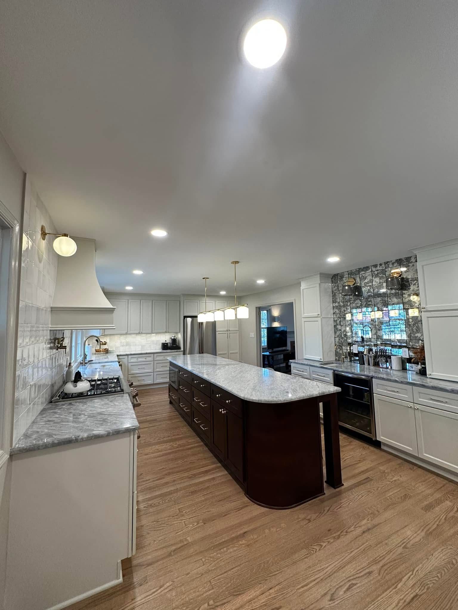 Bright, modern kitchen with a large island, white cabinets, granite counters, and wood flooring.