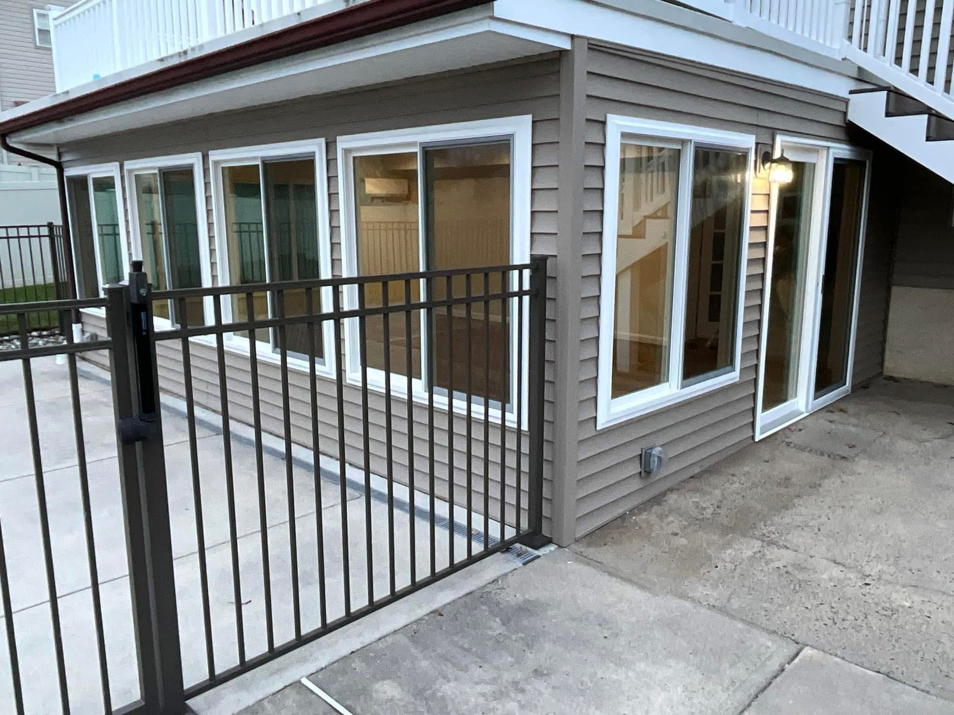 House entrance with white-trimmed windows, brown siding, and a black metal gate across the driveway