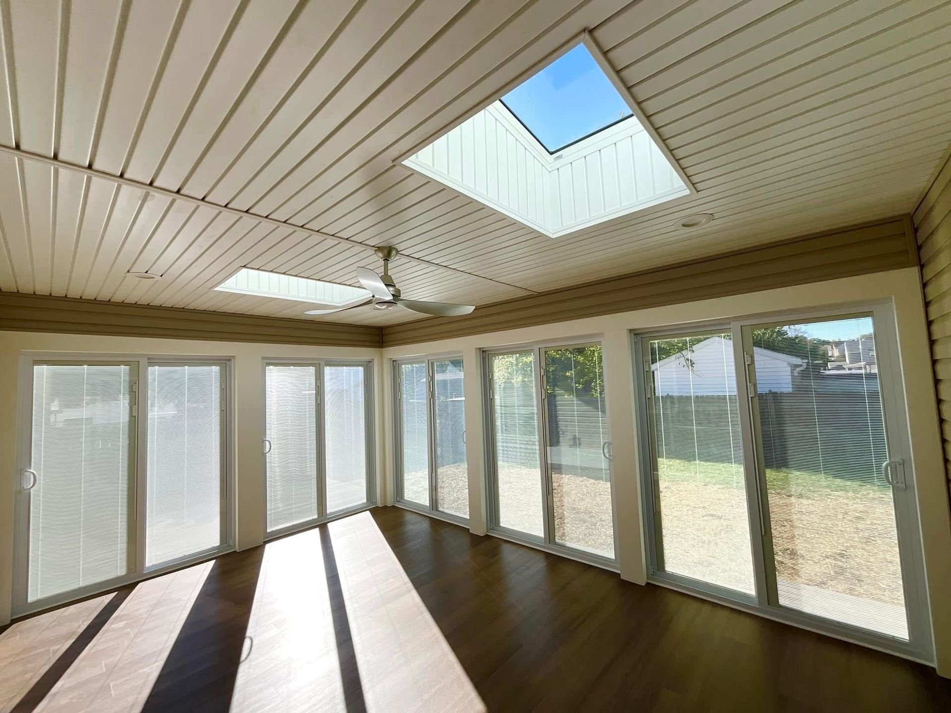 Bright sunroom with wood floor, skylight, ceiling fan, and large windows overlooking a yard