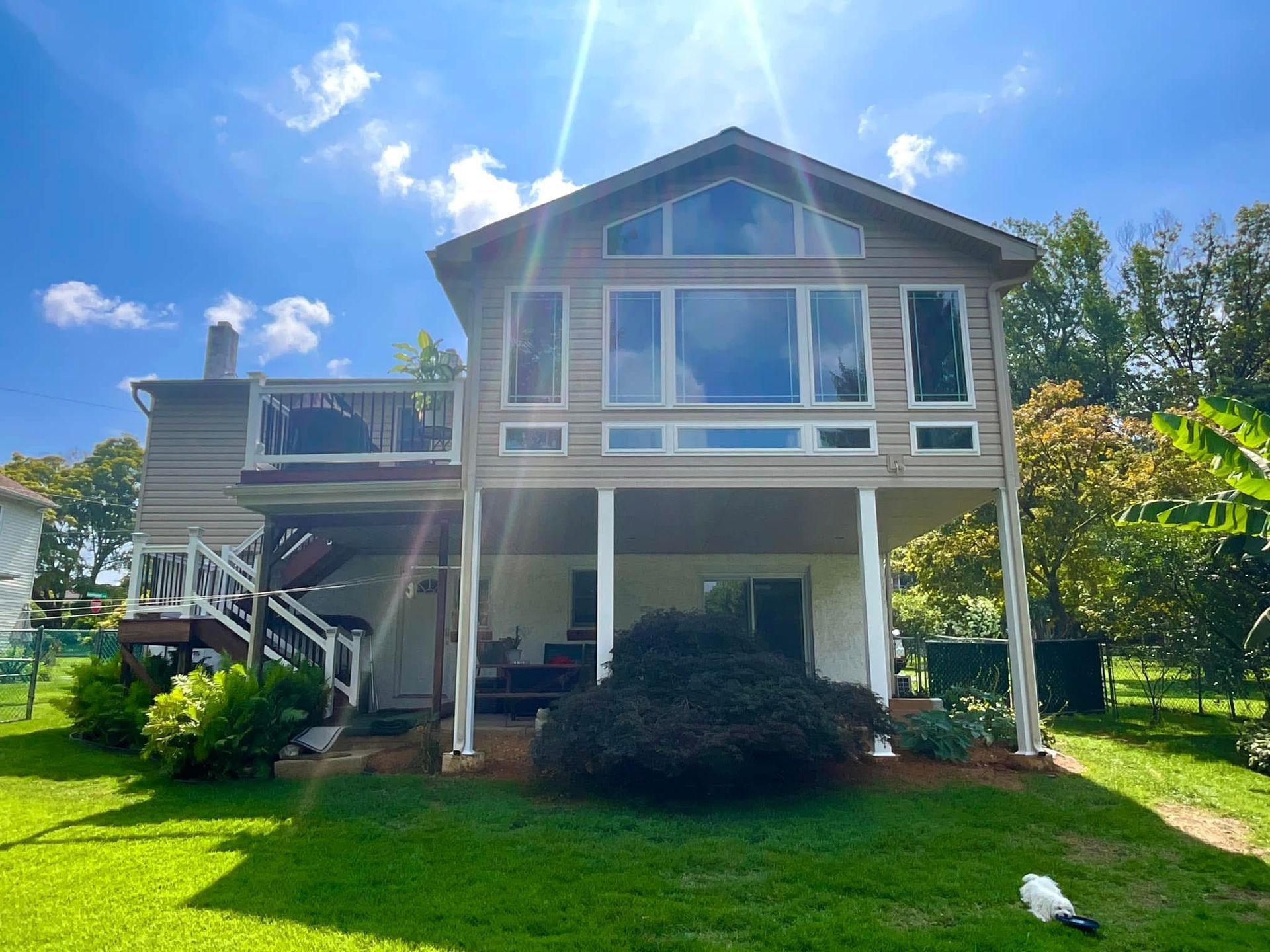 Two-story house with white columns, large windows, and a green lawn under a bright blue sky