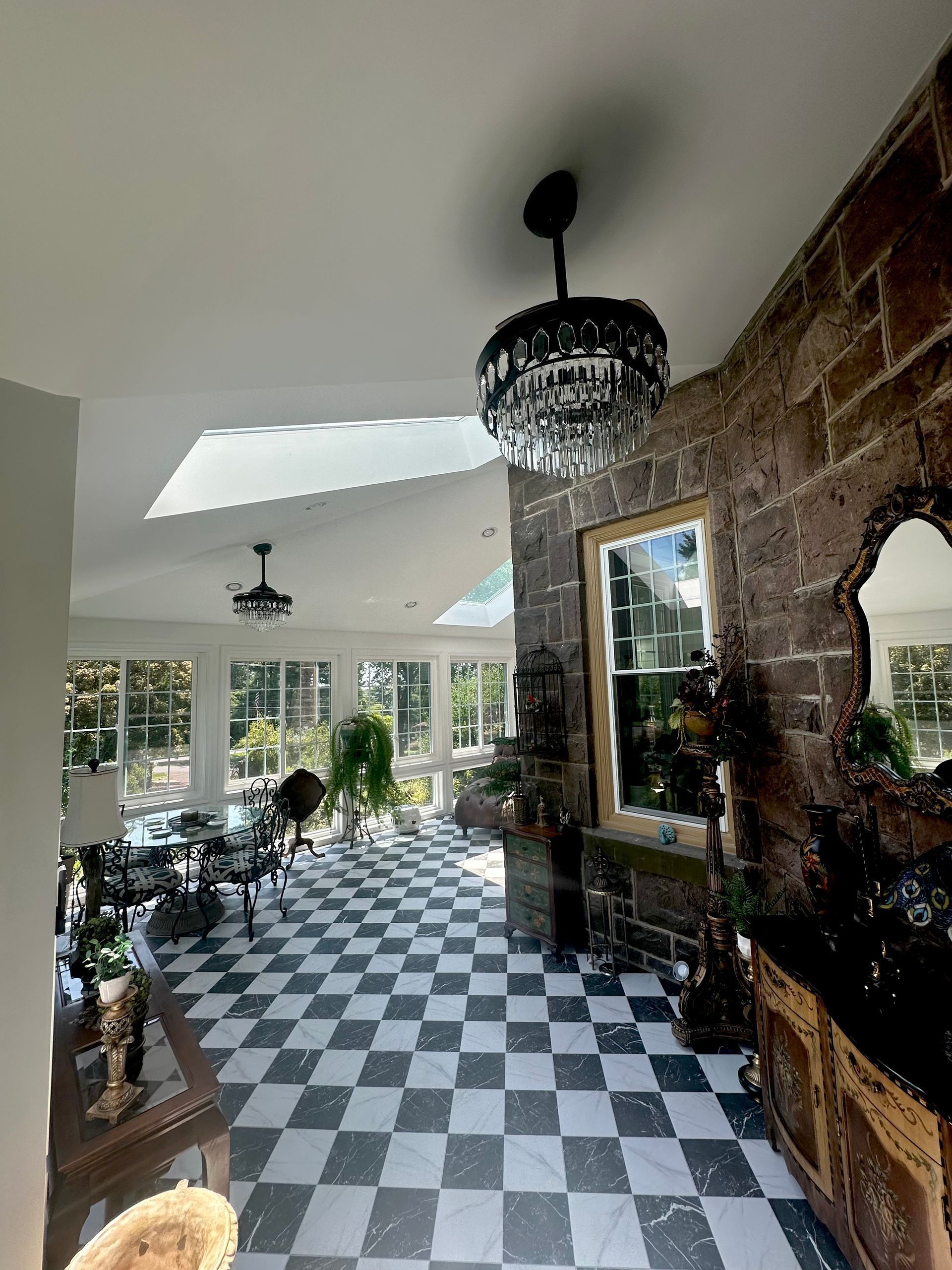 Bright sunroom with black-and-white checkered floor, brick wall, chandelier, and large windows opening to greenery.