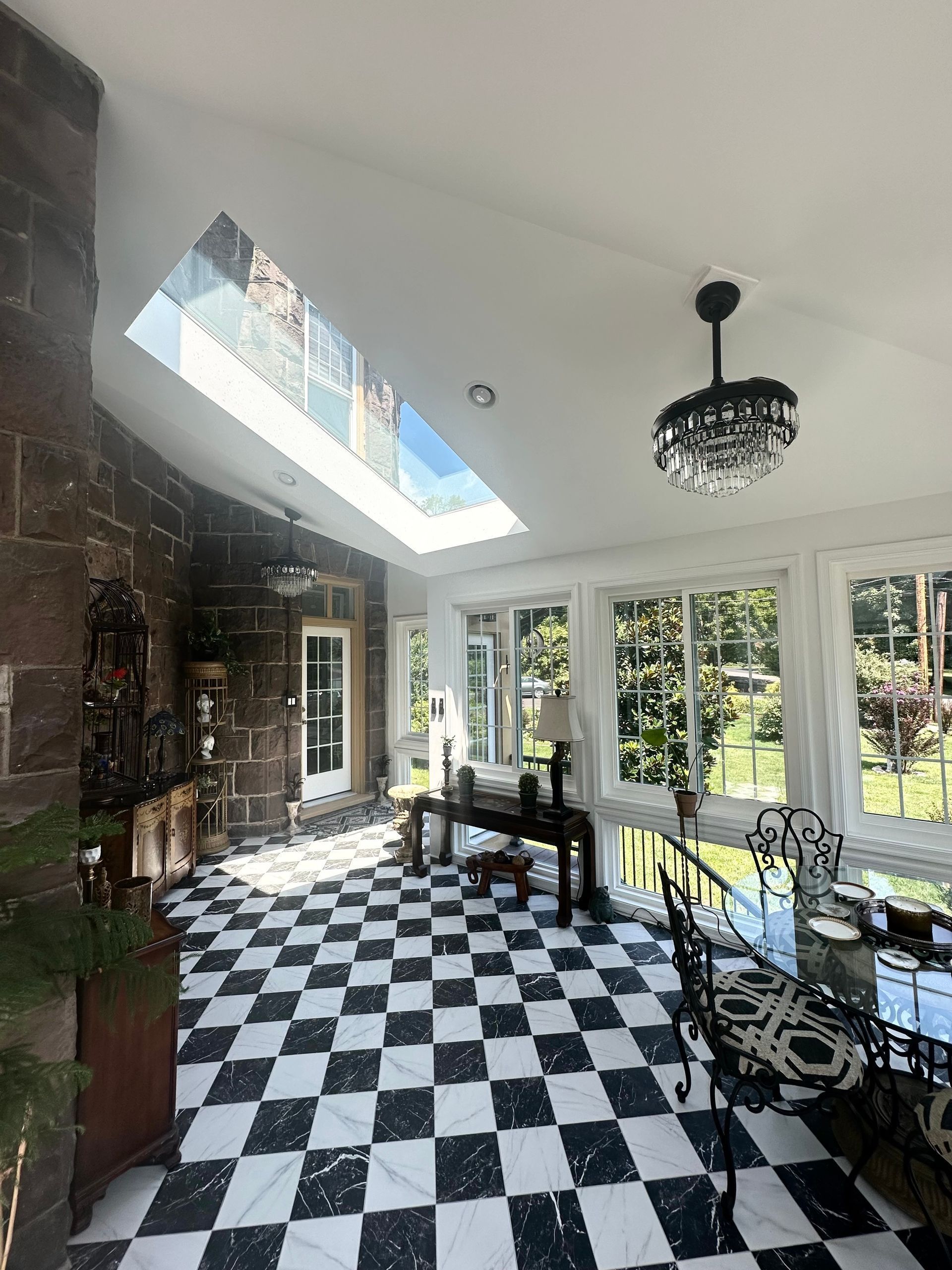 Sunlit patio room with black-and-white checkered floor, glass doors, and wrought-iron table and chairs