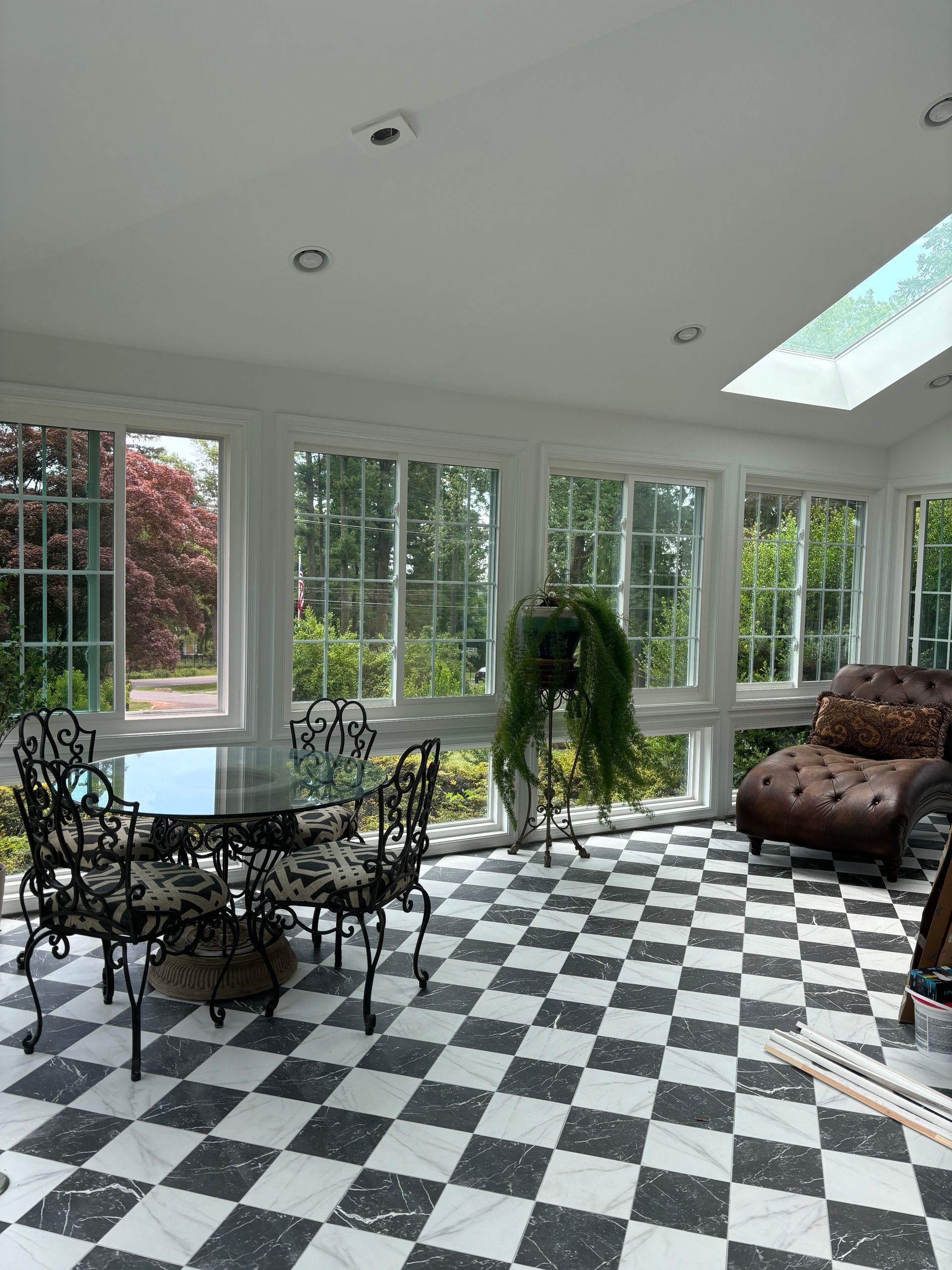 Sunroom with black-and-white checkered floor, glass walls, round table, chairs, couch, and skylight
