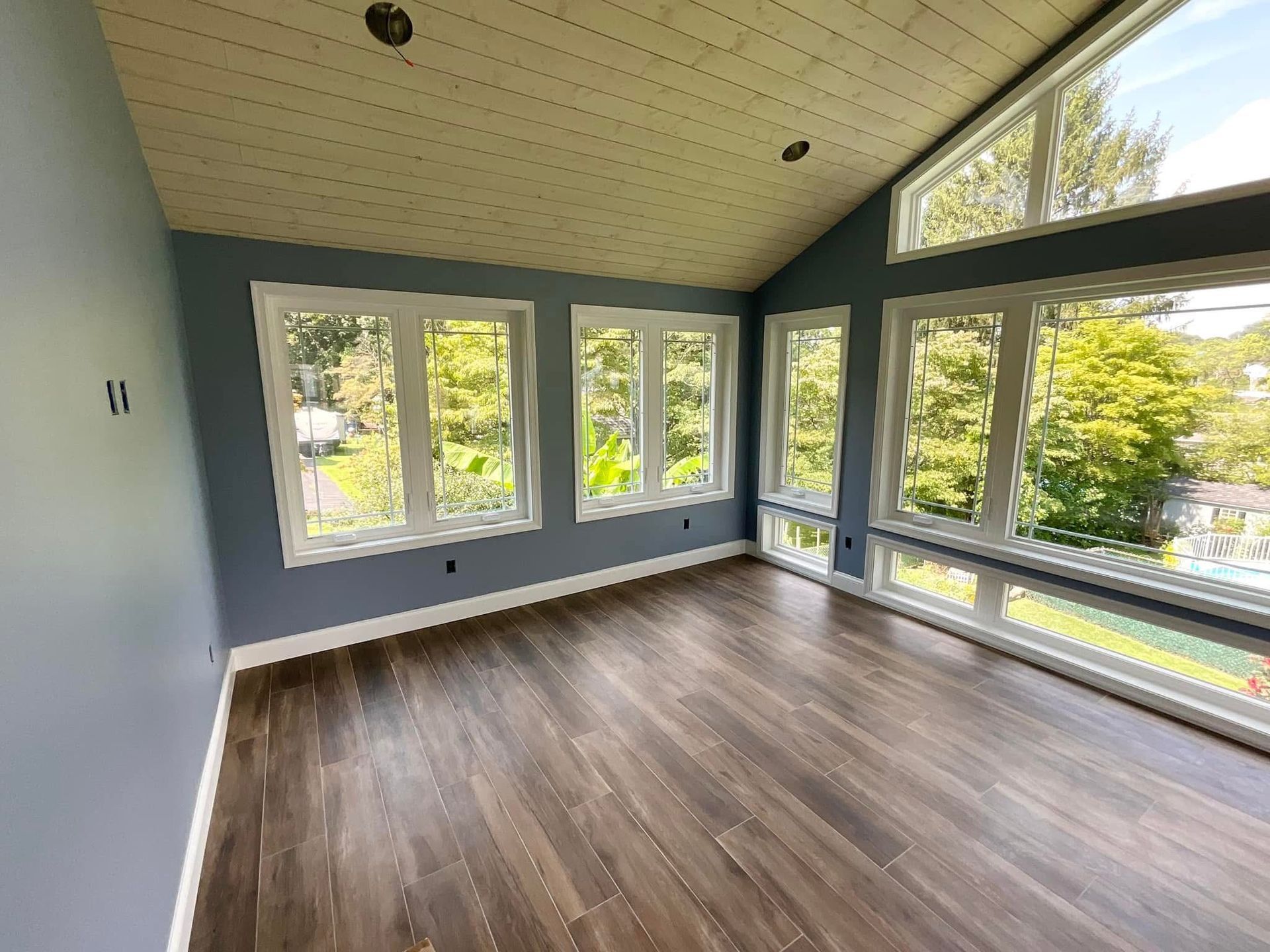 Empty bright room with large windows, wood floor, and light blue walls.