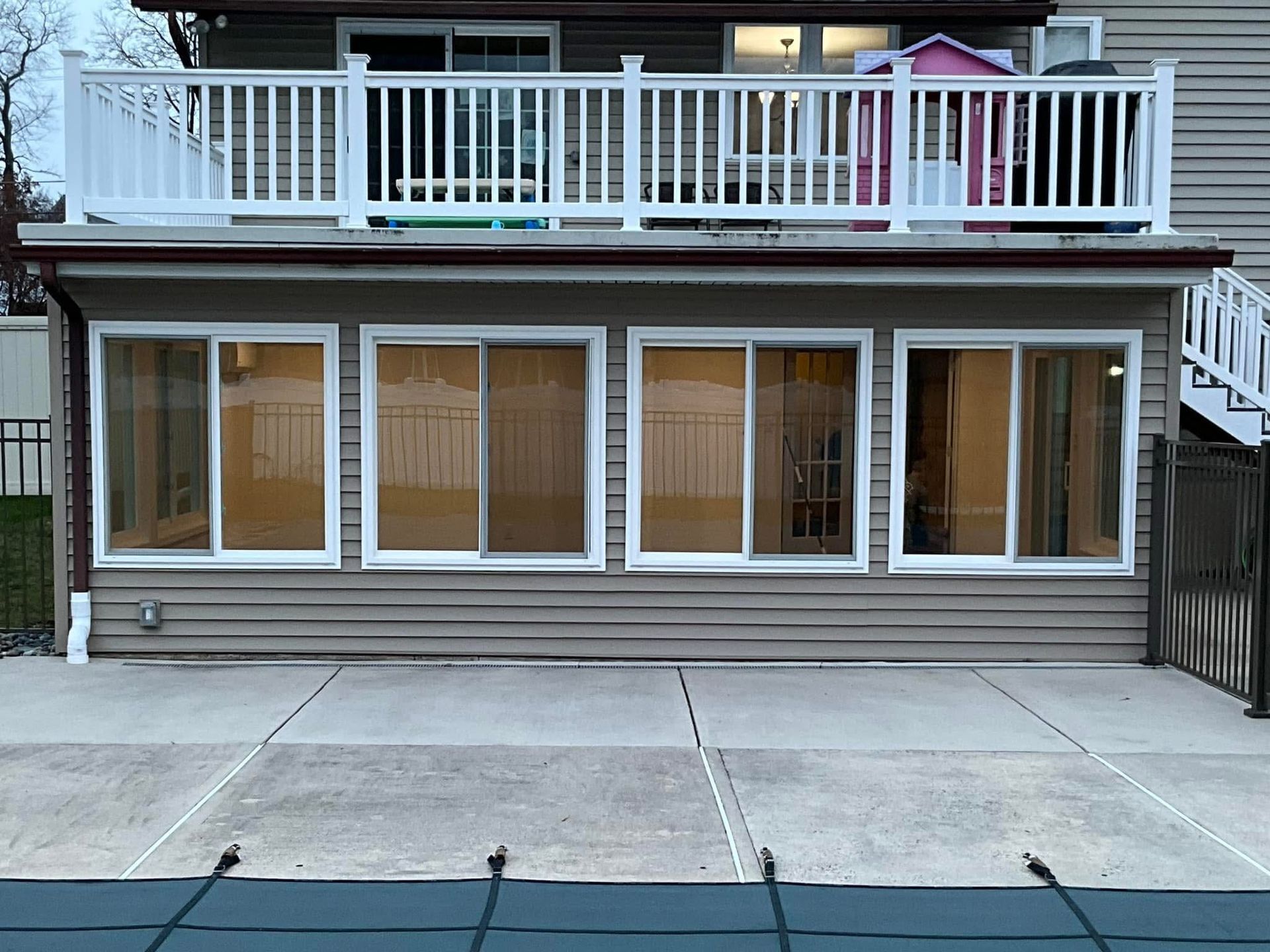 Two-story house with white deck railing, large windows, and a concrete driveway in front