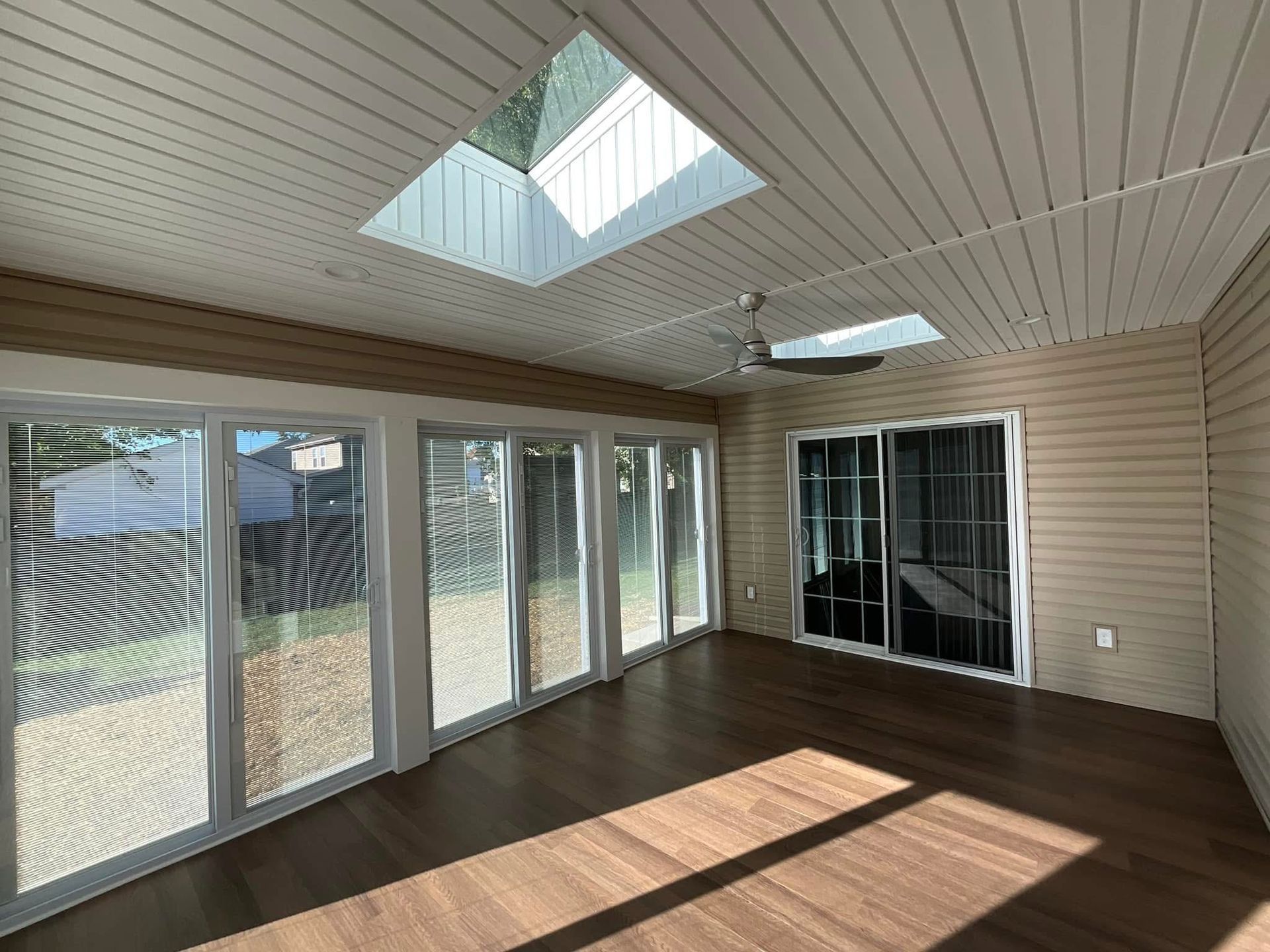 Bright sunroom with skylights, glass doors, white paneled ceiling, and dark wood floor.