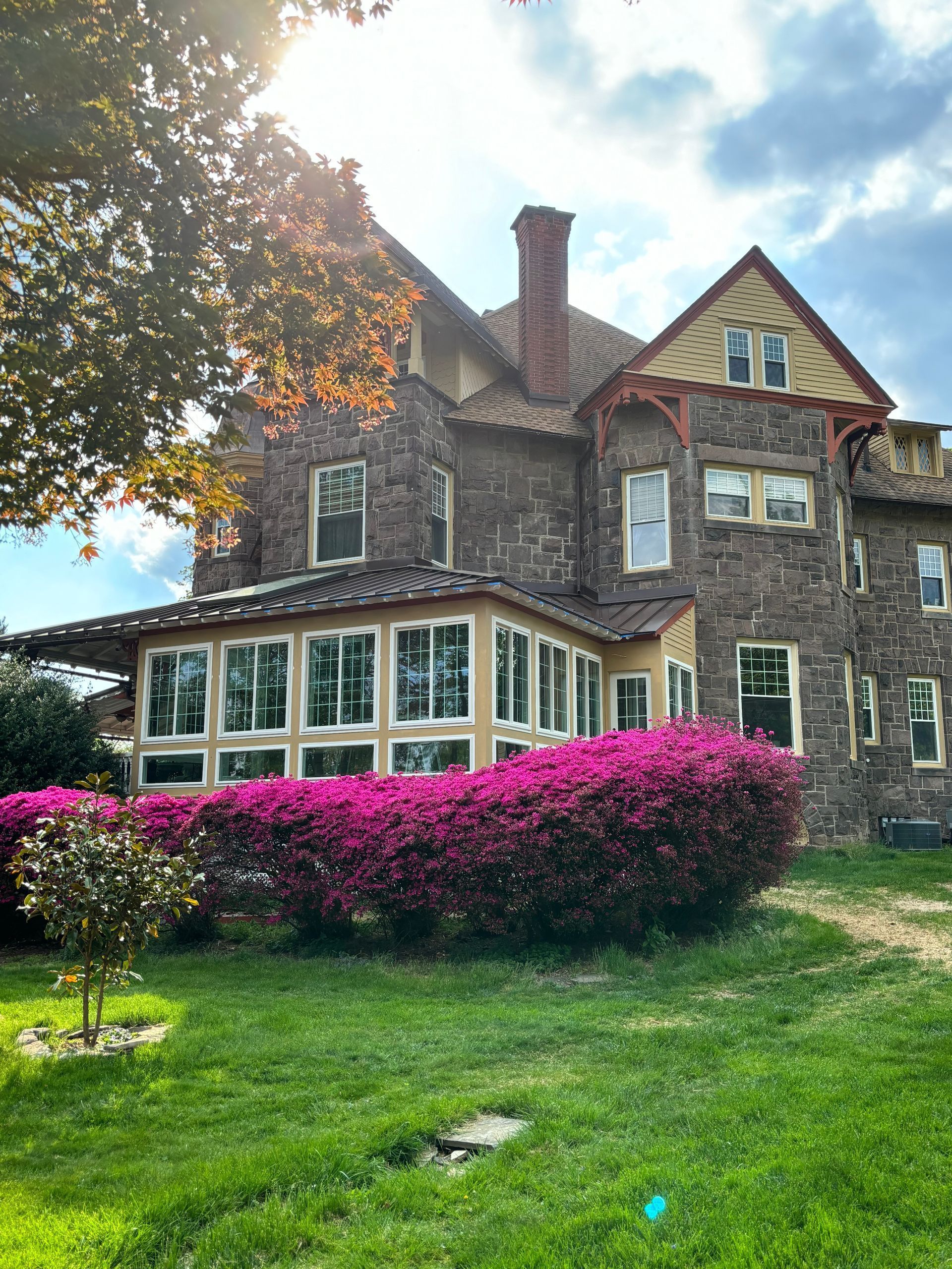 Stone house with red roof and pink flowering hedge in a sunny green yard