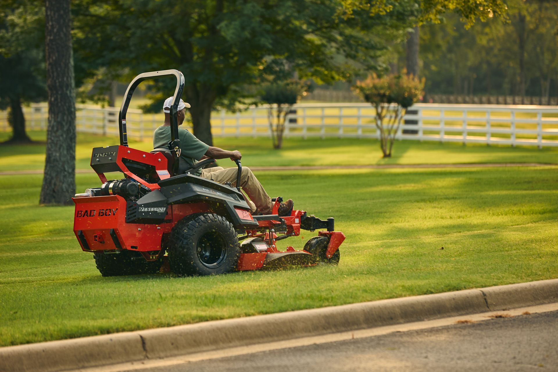 Person mowing a bright green lawn on an orange riding lawnmower on a sunny day.
