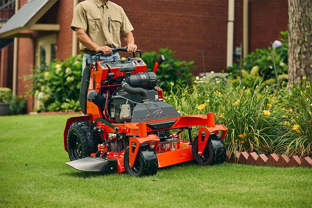 Person mowing lawn with a red zero-turn mower in a yard near a house.
