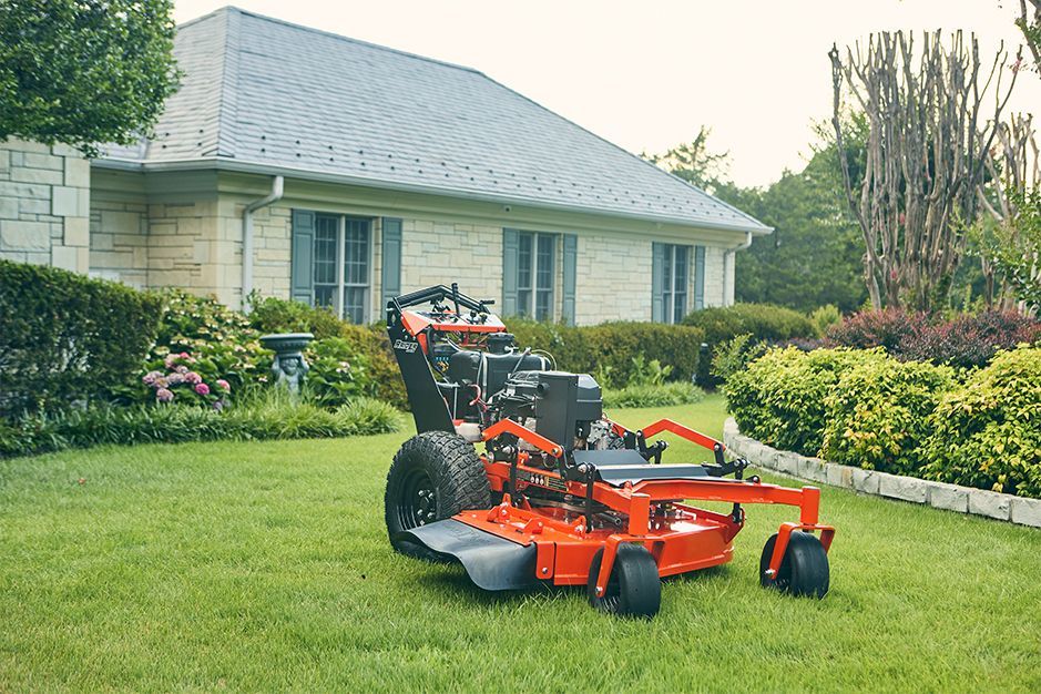 Orange zero-turn mower on a green lawn in front of a light-colored house.