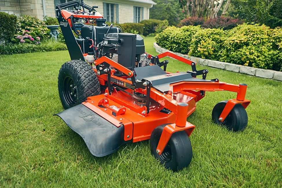 Orange zero-turn lawnmower on a green lawn, next to a house and garden.
