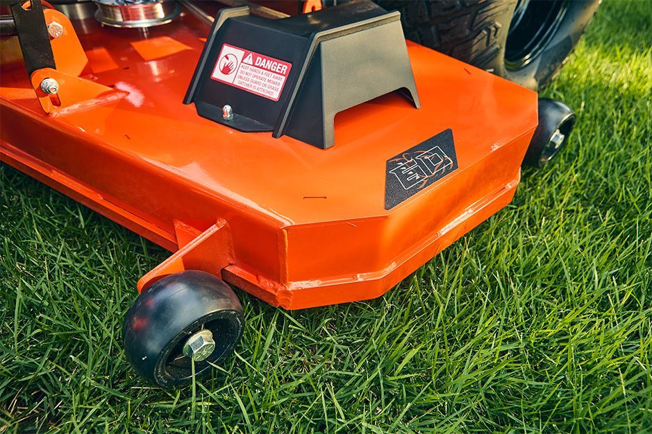 Orange riding lawn mower deck on green grass. A black safety cover is in the center.
