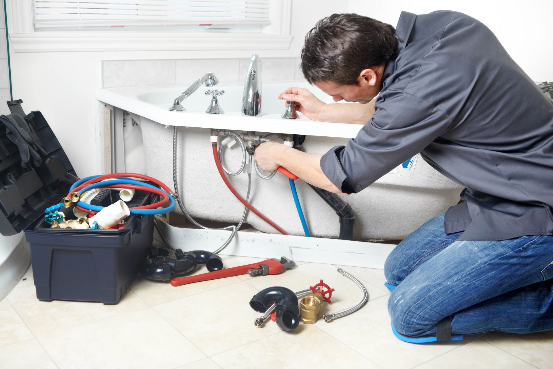 Plumber repairing pipes under a bathroom sink with tools and a toolbox nearby