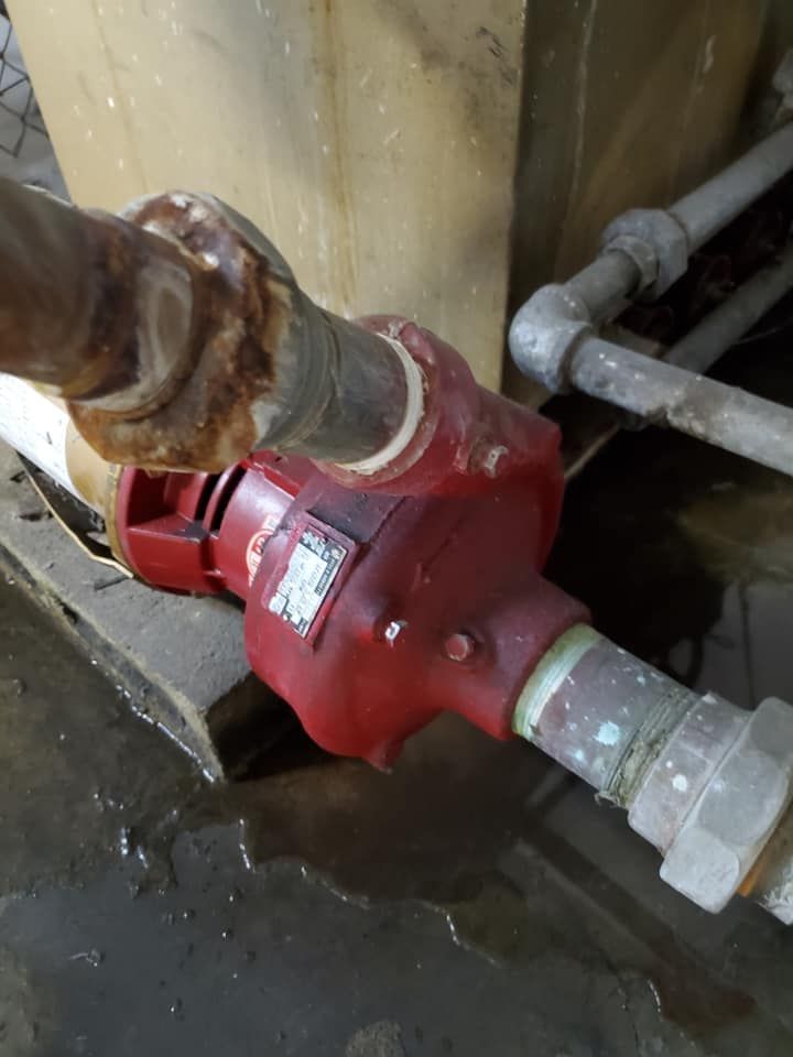 Red water pump connected to metal pipes in a damp industrial area