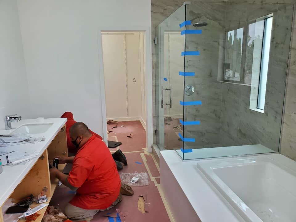 Worker installing cabinetry in a bathroom under renovation, with tools and debris on the floor.