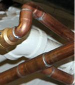 Copper and white pipes with elbow joints in a close-up plumbing installation.