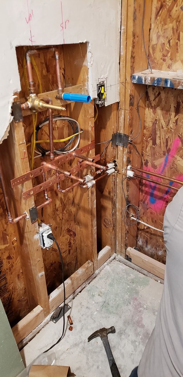 Partially stripped bathroom wall with exposed plumbing, a sink, and a hammer on the floor