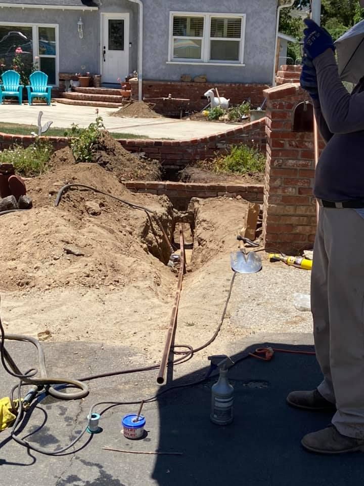 Backyard excavation beside a house, with exposed dirt trench and a worker standing nearby