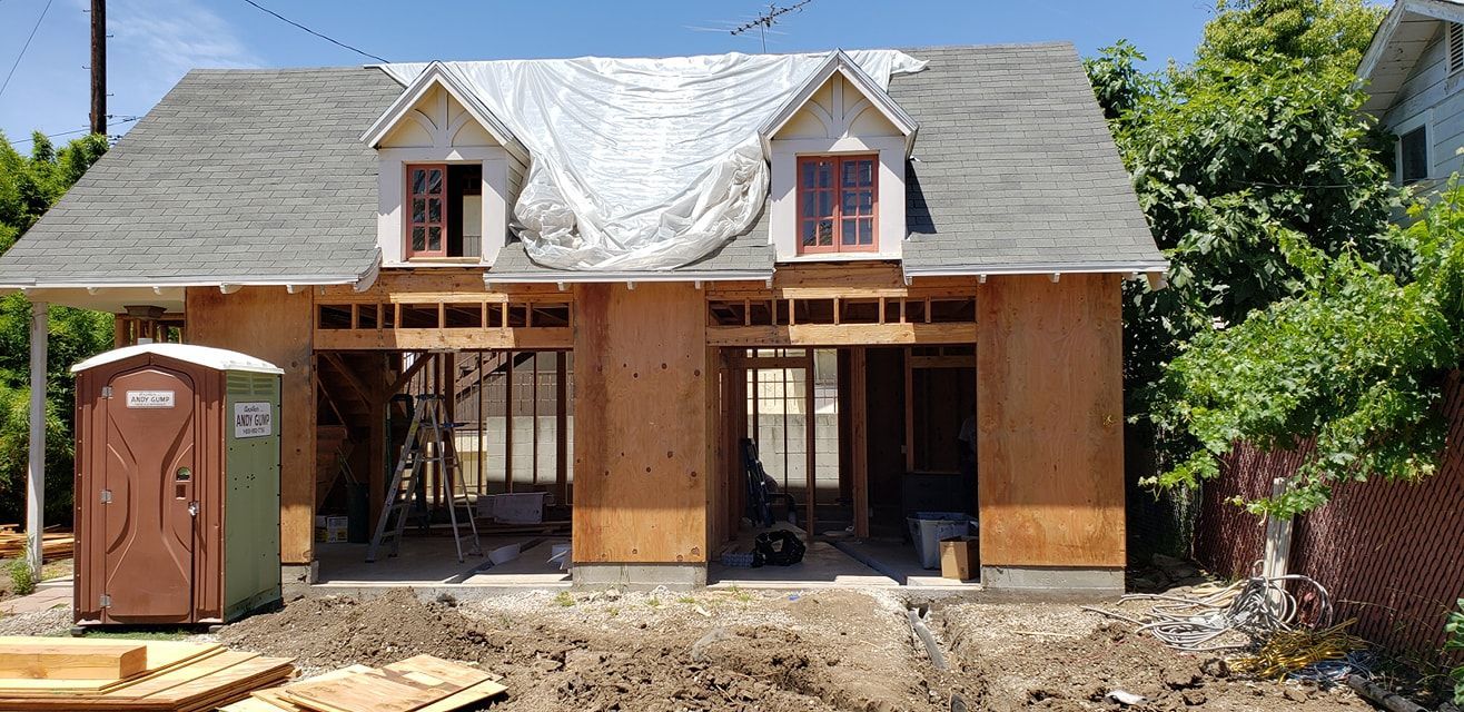 Partially finished two-story house with scaffolding and portable toilet in front yard