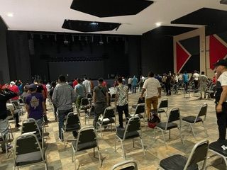 A group of people are standing in a large room with chairs.