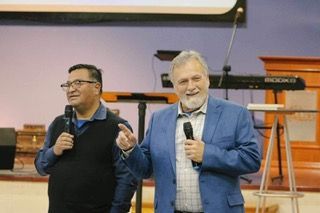 Two men are standing next to each other holding microphones in a church.