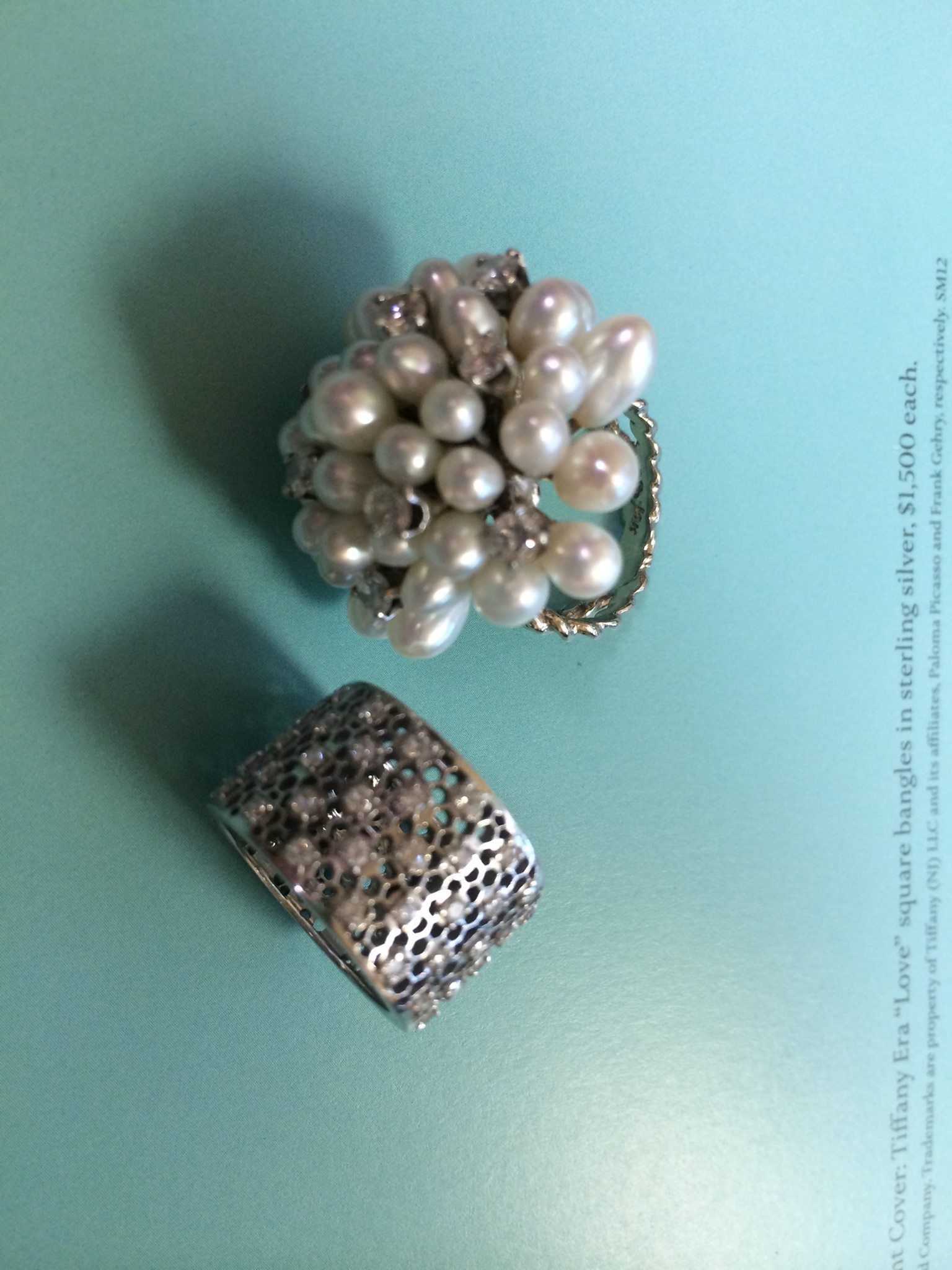 Two rings on a blue surface: one with pearls, the other studded with small stones.