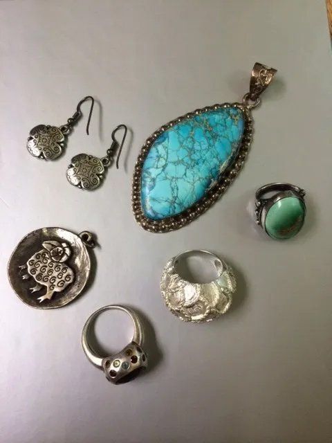 Silver jewelry: earrings, pendant with turquoise stone, rings, and charm on a gray surface.