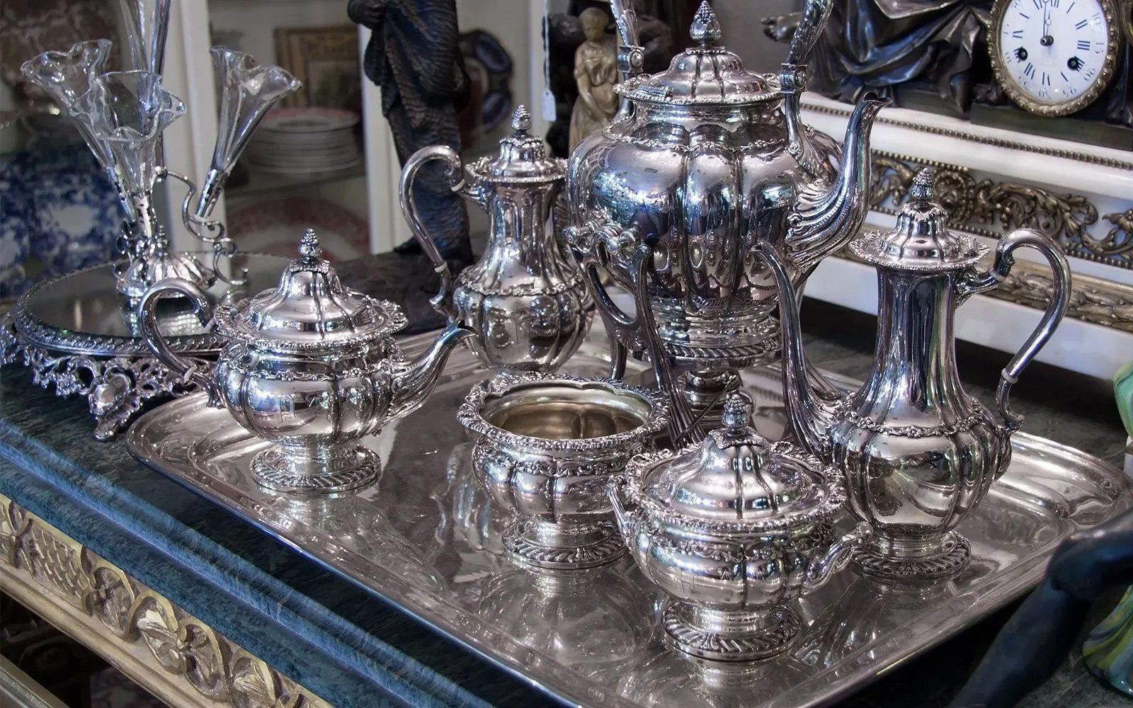 Silver tea service on a silver tray, including a teapot, sugar bowl, and creamer.