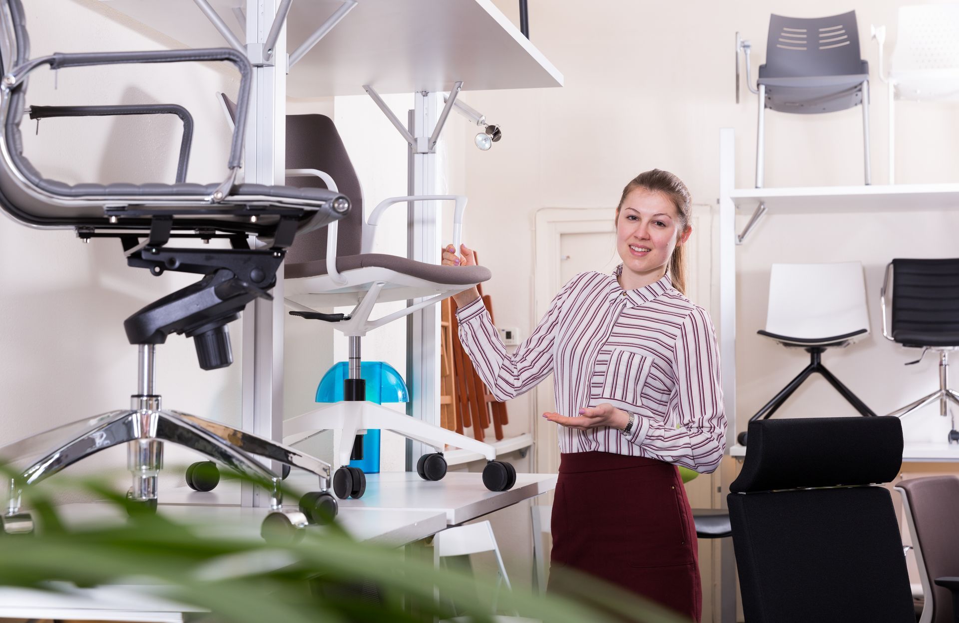 Woman standing in a modern office furniture showroom beside stacked chairs and shelves