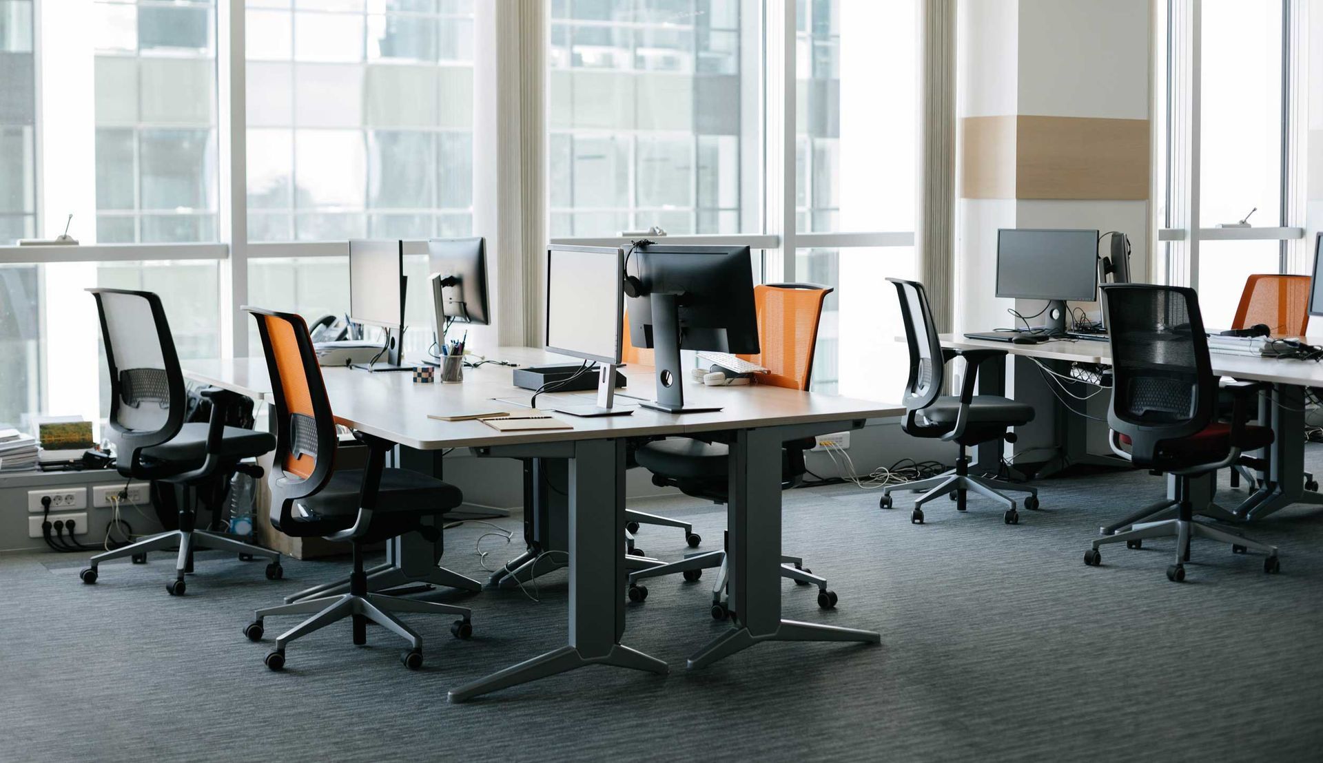 Modern office with desks, black chairs, computer monitors, and large windows
