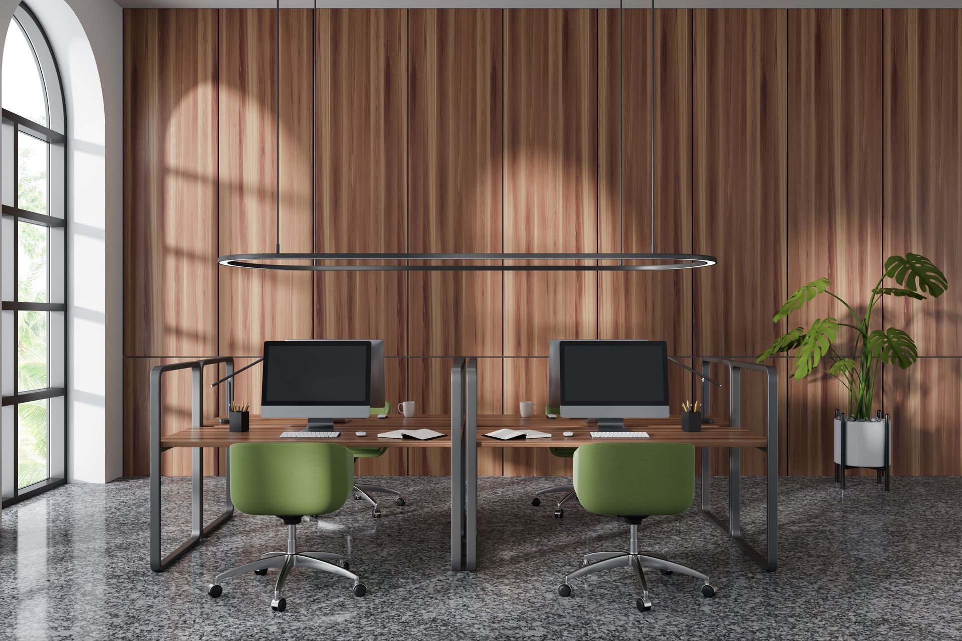Modern office workspace with two desks, computers, green chairs, wood panel walls, and a large window.