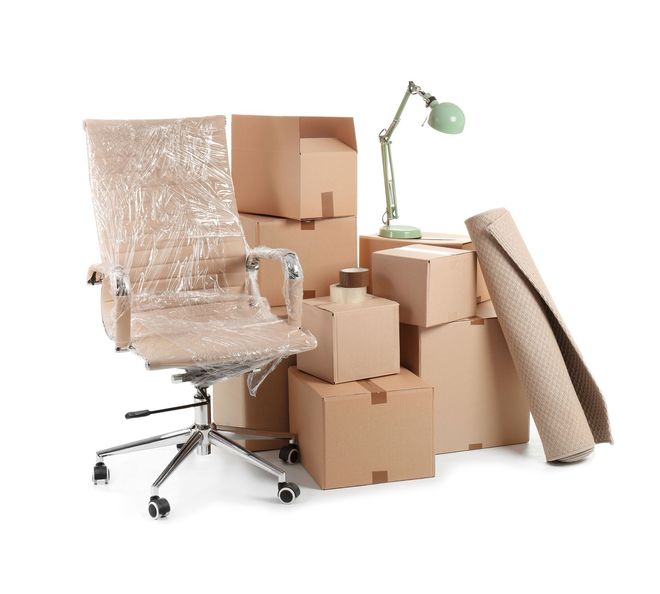 Packed office chair, cardboard moving boxes, rolled rug, and green desk lamp on a white background