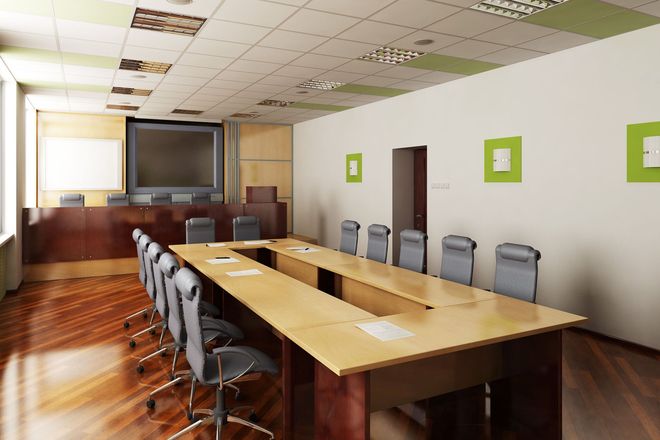 Conference room with long wooden table, chairs, wall-mounted screen, and bright windows