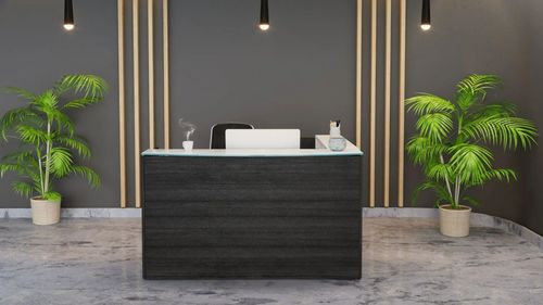 Modern office reception desk with black front panel, white top, and potted plants against a dark wall.