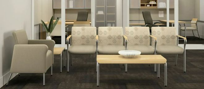 Modern waiting room with beige chairs, a wooden coffee table, and shelves in the background