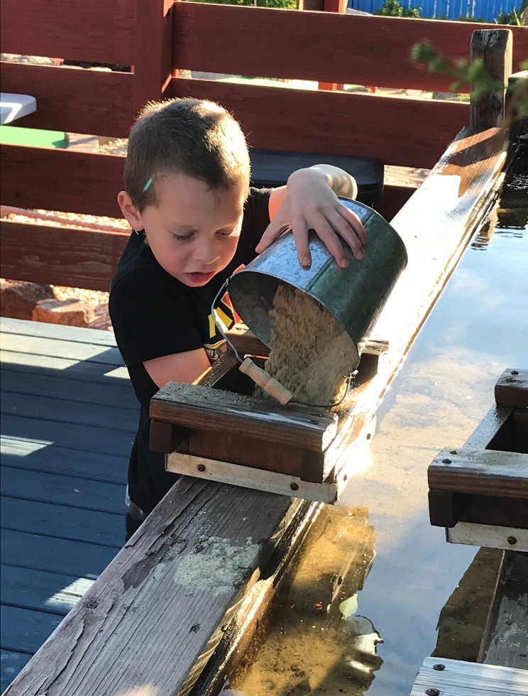 A young boy is pouring water from a bucket onto a wooden board.