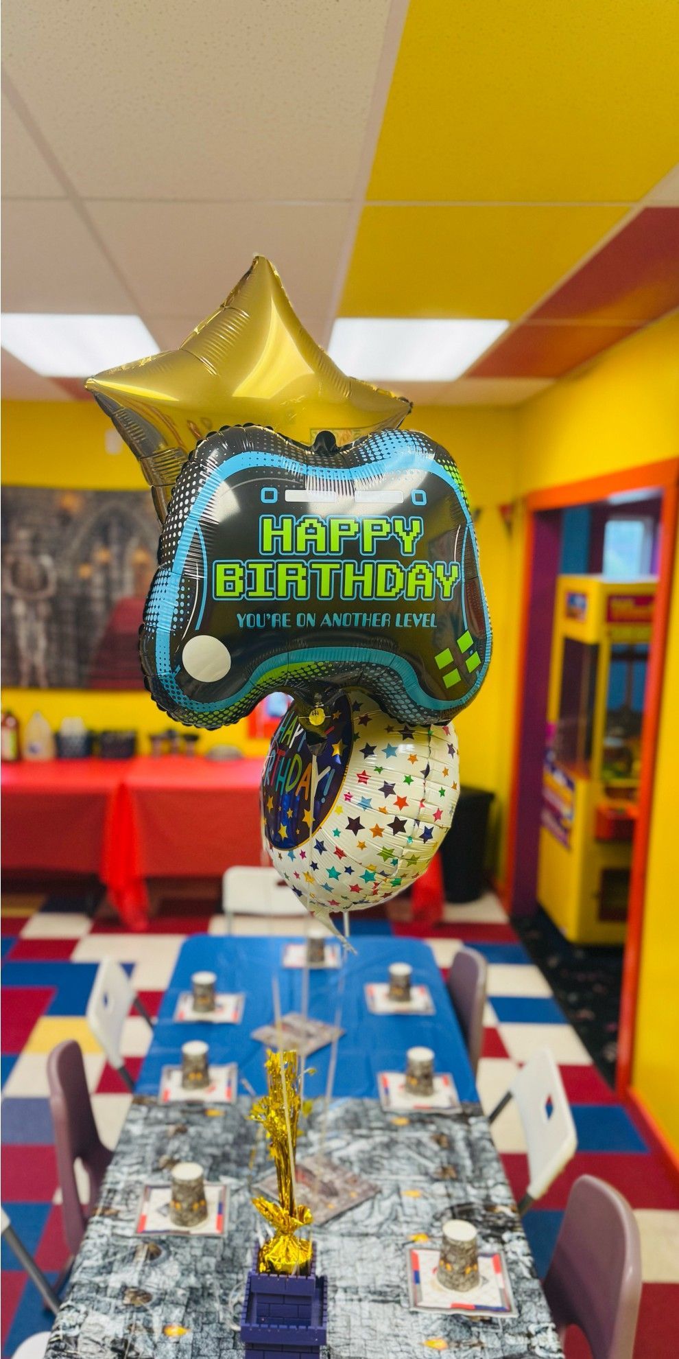 Birthday party table with balloons shaped like a game controller. Colorful room.
