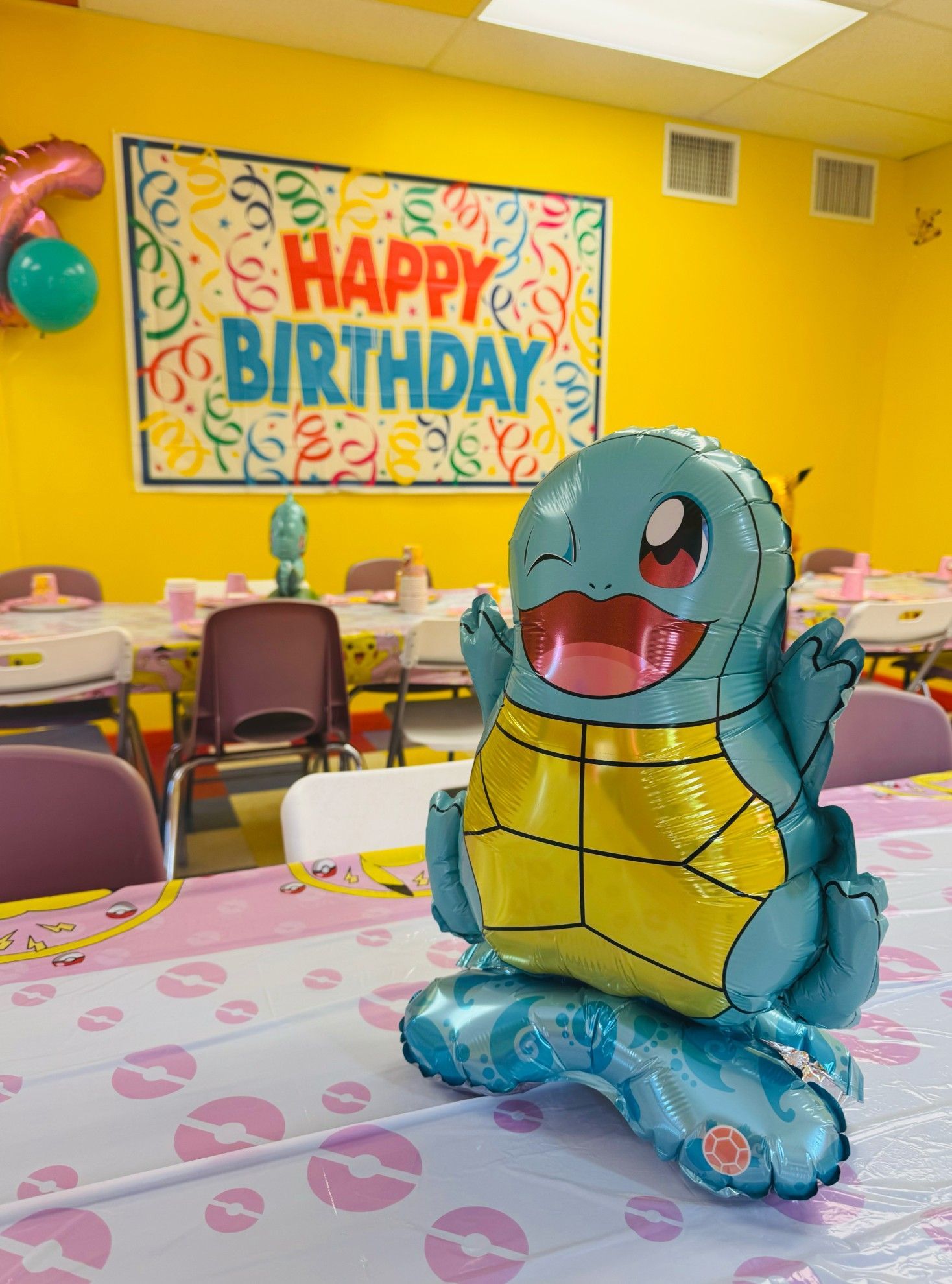 Squirtle balloon centerpiece at a birthday party, table with pink tablecloth, yellow walls.