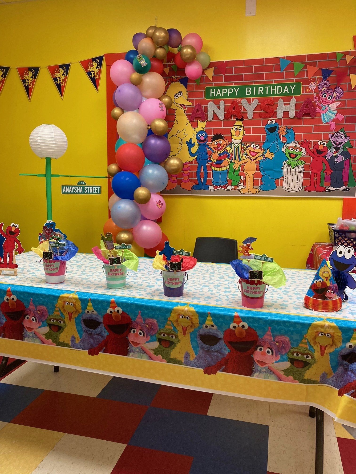 A table with a sesame street tablecloth and balloons on it