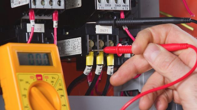 Hand testing electrical wires with a multimeter. Yellow meter displays 0.00 volts.