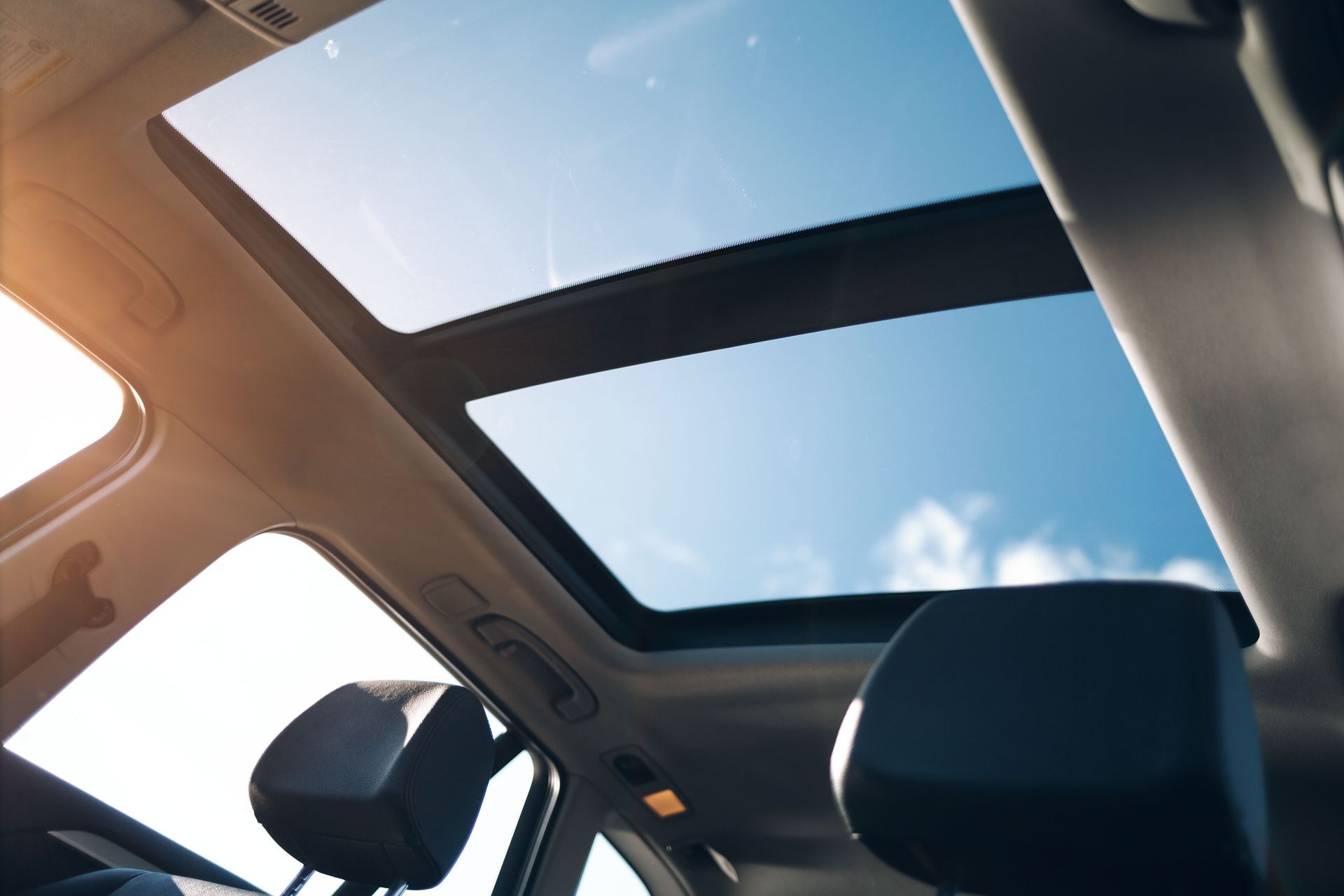 Car interior with open sunroof showing blue sky and sunlight