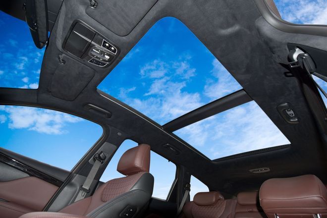 Luxury car interior with brown seats and panoramic sunroof showing a blue sky