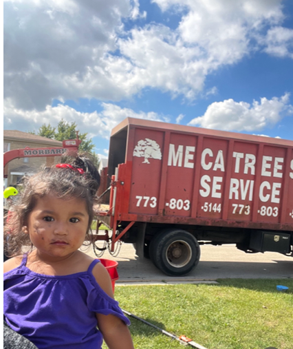 A little girl standing in front of a meca tree service truck