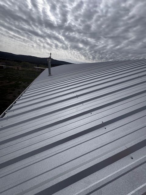 Metal rooftop with a vent chimney under a cloudy sky, seen from above