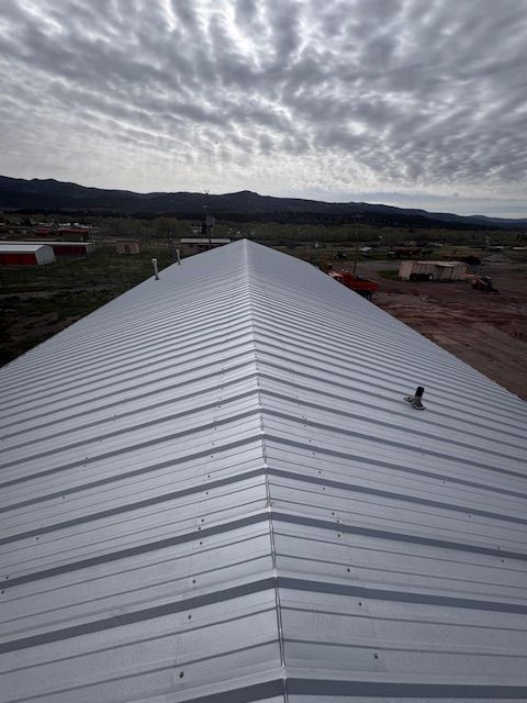 Long white metal roof under cloudy sky, with mountains and buildings in the distance