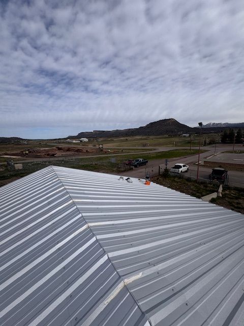 Silver metal roof in foreground with rural fields and a hill under a cloudy sky.