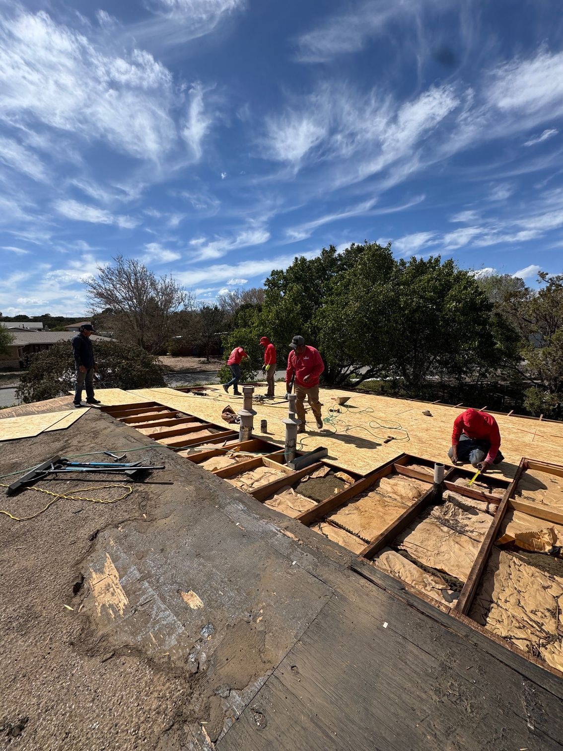 Workers laying wooden framing on a rooftop under a bright blue sky.