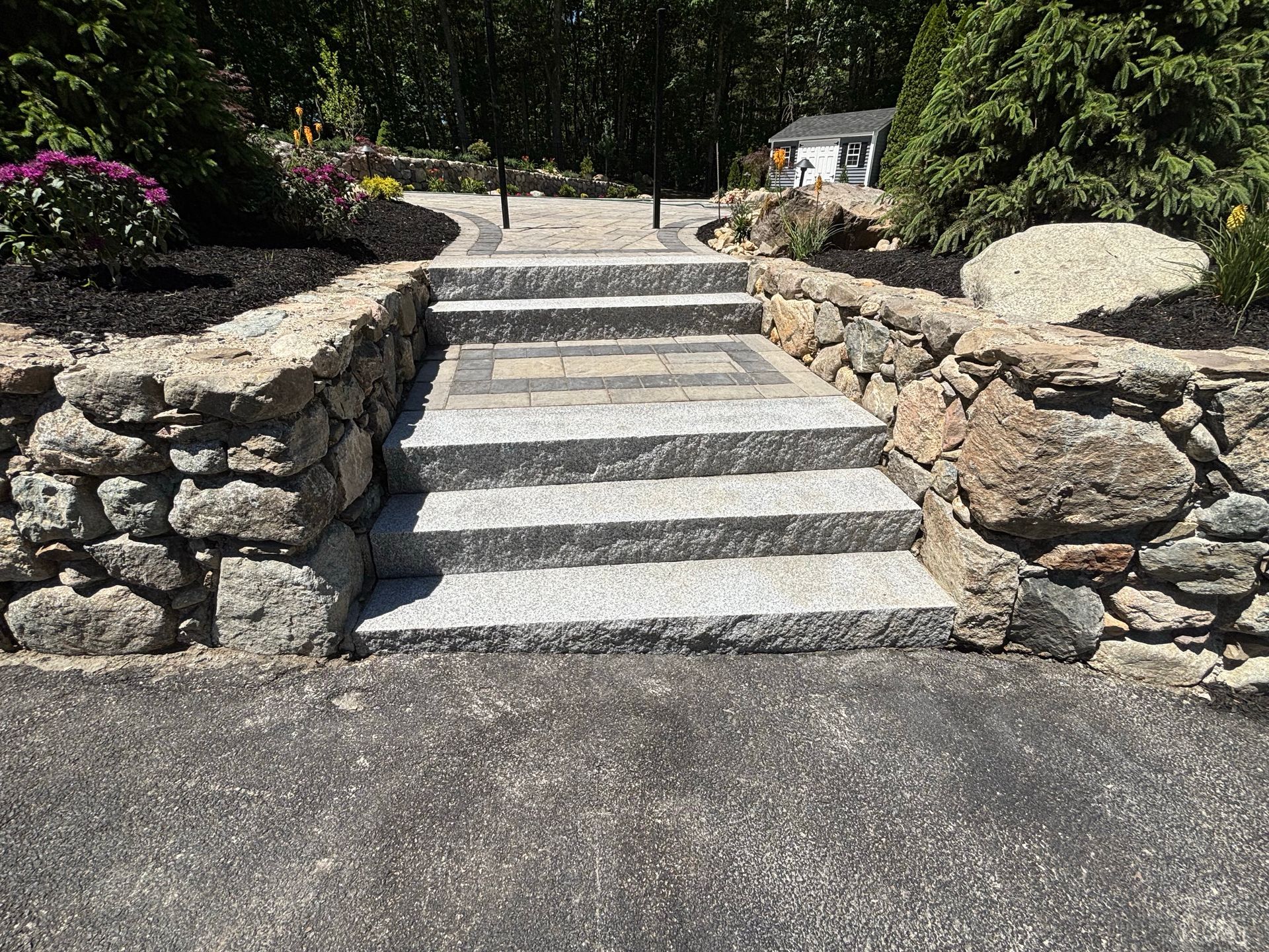 Stone steps and a ramp between low rock walls leading up a garden path.
