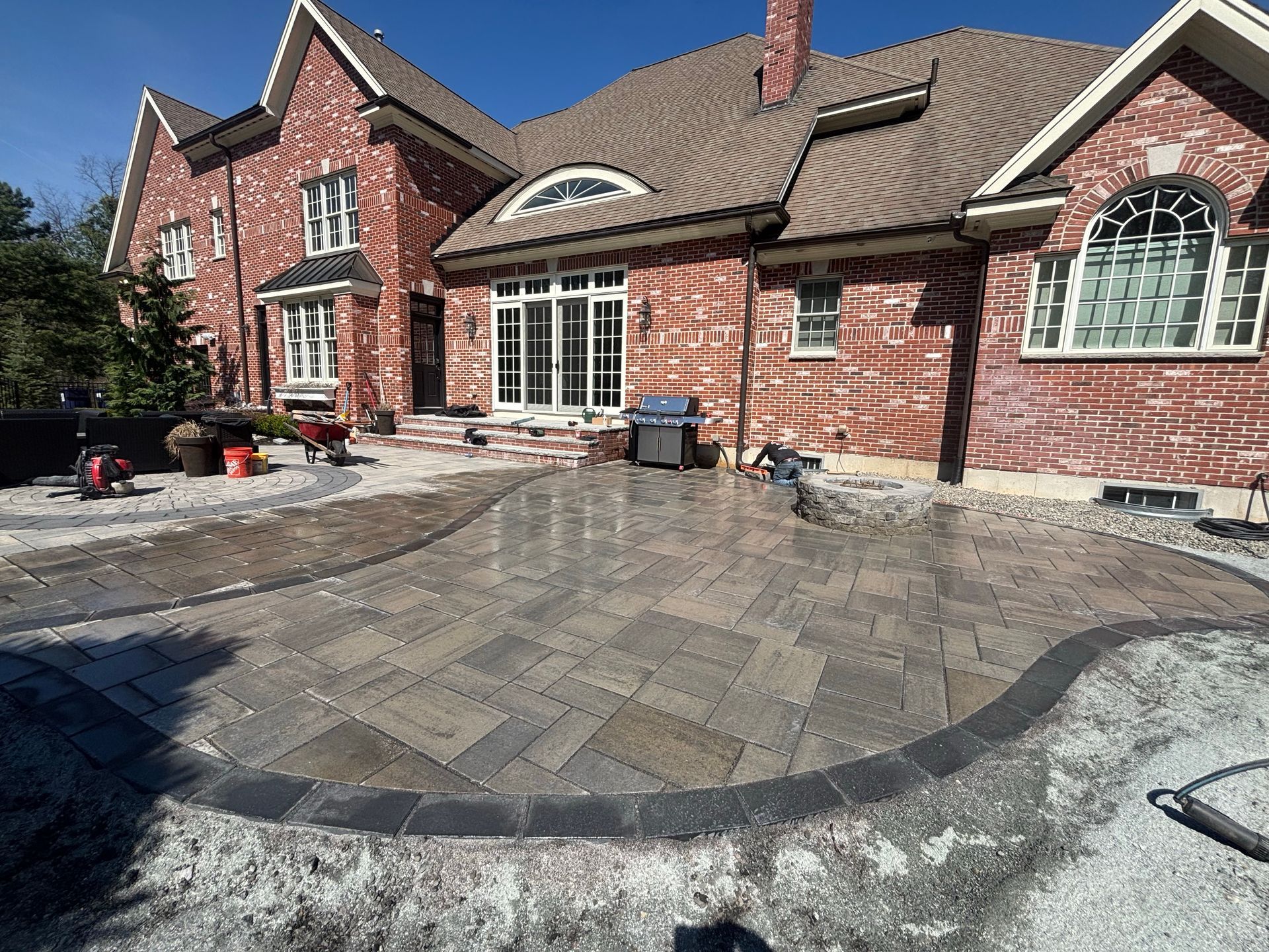 Brick patio and curved paver walkway in front of a red brick house with white-framed windows.