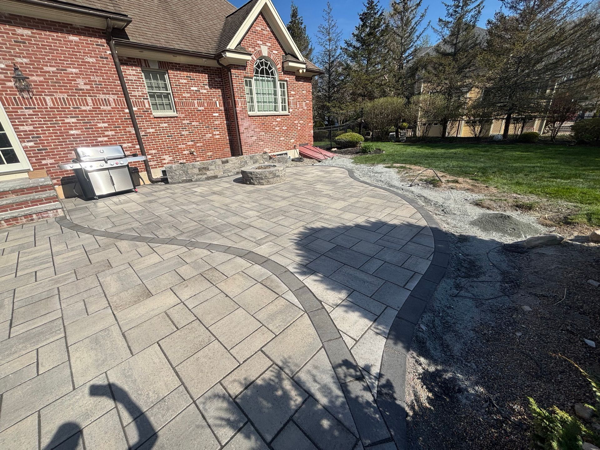 Brick patio beside a house, with a curved paver walkway and gravel edging in a sunny yard